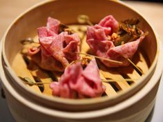 small food items in a wooden bowl on a table top with chopsticks and seasoning