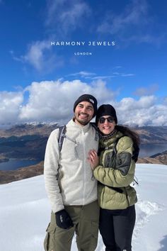 a man and woman standing on top of a snow covered slope next to each other