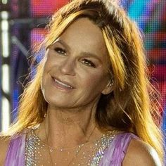 a woman with long blonde hair wearing a purple dress and smiling at the camera while standing in front of a colorful background