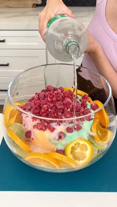 a woman pouring water into a bowl filled with fruit and ice cream, on top of a counter