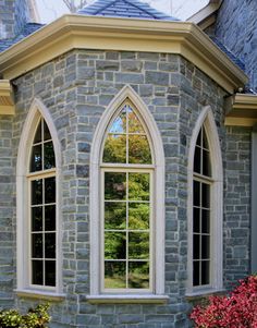 an arched window on the side of a stone building with red flowers in front of it