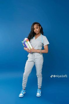 a woman in grey scrubs and sneakers is holding some books while standing against a blue background