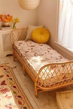 a small bed sitting next to a window in a room with white walls and wooden flooring