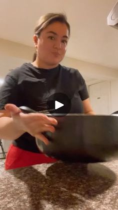 a woman sitting at a kitchen counter holding a pan