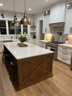 a large kitchen with white cabinets and wood flooring on the countertops, two pendant lights hanging over the island