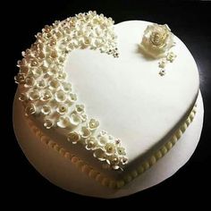 a heart shaped cake with white frosting and flowers on the top is decorated with pearls