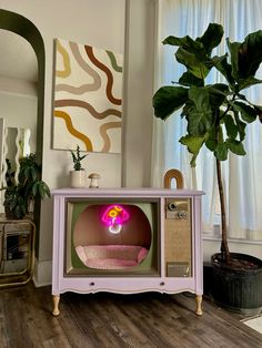 a pink tv set sitting on top of a wooden floor next to a potted plant