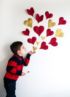 a young boy holding onto some hearts on a white wall with red and gold foil