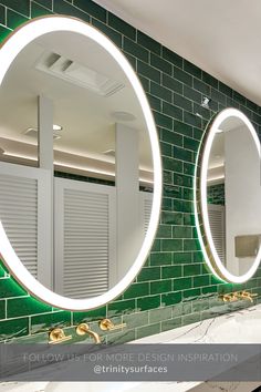 two round mirrors are on the wall in front of a green tiled bathroom countertop