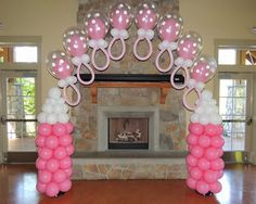 an arch decorated with pink and white balloons in front of a fireplace at a party