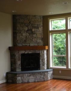 an empty living room with a stone fireplace and large windows in the wall, along with hard wood flooring