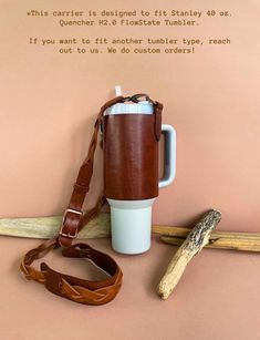 a coffee cup with a brown leather strap sitting on top of a table next to a wooden stick