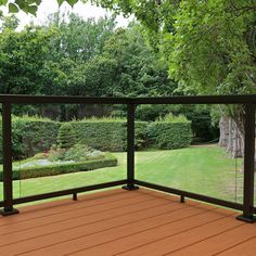 a wooden deck with metal railings in front of a garden and trees on the other side