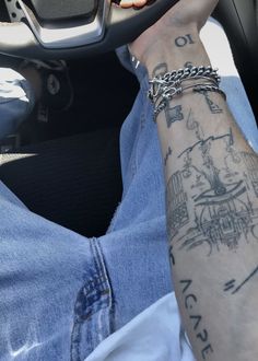 a person with tattoos on their arm holding a steering wheel and wearing a chain bracelet