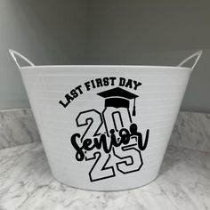 a white bucket with the words last first day on it and a graduation cap in black