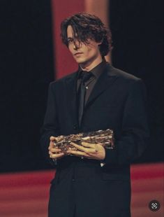 a male in a black suit and tie is holding a piece of wood with his hands