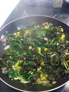 spinach and onions cooking in a wok on the stove top, with seasoning