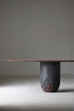 a wooden table sitting on top of a cement floor next to a white wall in an empty room