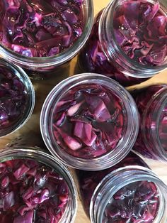 several jars filled with red onions on top of a wooden table