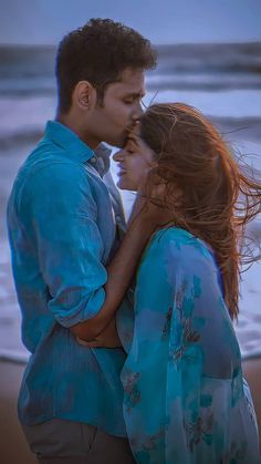 a man and woman standing next to each other in front of the ocean at sunset