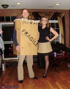 a man and woman standing in a living room holding a cardboard sign that says fragile