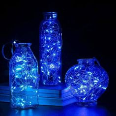 three glass vases with fairy lights in them on a table next to a stack of books