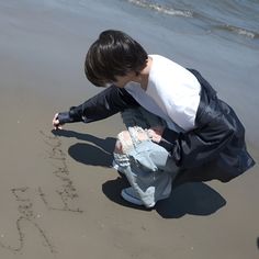 a young boy is writing in the sand at the beach with his name written on it