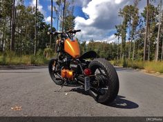 an orange motorcycle parked on the side of a road in front of some tall trees