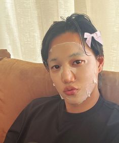 a man with white patches on his face sitting in front of a brown couch wearing a black t - shirt