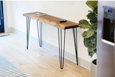 a wooden table with hairpin legs and a cell phone on it next to a plant