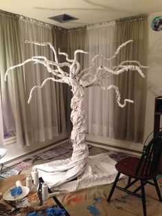 a paper mache tree sitting on top of a table next to a chair and window