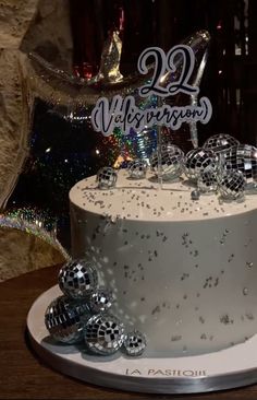 a white cake sitting on top of a table covered in silver and black confetti