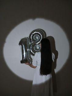 a woman holding a large balloon in front of a wall with the number thirteen on it