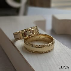 two gold wedding rings sitting on top of a white table next to each other with the words love written on them