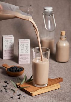 a person pouring milk into a glass on top of a wooden cutting board next to other ingredients