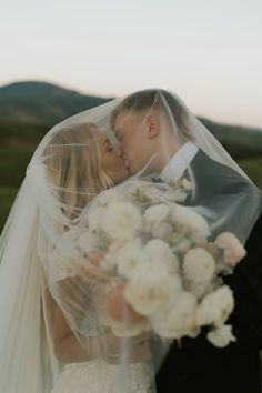 a bride and groom kissing under a veil