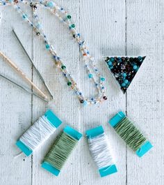 several crafting supplies are laid out on a white wooden surface, including yarn, needles and beads