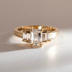 a yellow gold ring with three baguetts of diamonds on the side, sitting on a white surface