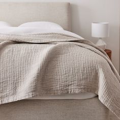 an unmade bed with white linens and a beige comforter on the headboard