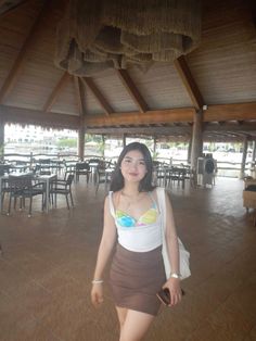 a woman in a brown skirt and white tank top is standing under a straw roof