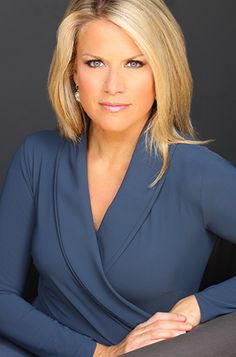 a woman with blonde hair wearing a blue top and posing for a photo in front of a black background