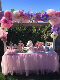 a table topped with lots of cake and cupcakes covered in pink and purple flowers