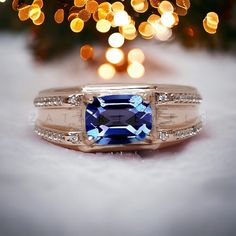 a ring with a blue stone surrounded by diamonds on a white furnishing next to a christmas tree