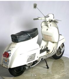 a white motor scooter parked on top of a cement floor next to a wall