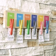 several colorful pieces of paper hanging from hooks on a stone wall with name tags attached to them