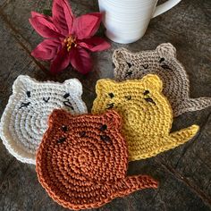 three crocheted cats sitting next to a coffee cup