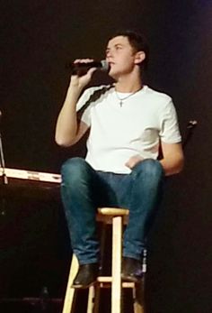 a man sitting on top of a wooden stool while holding a microphone in his hand