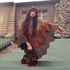 a woman is standing on some steps with her hand in her pocket and wearing a brown cape