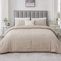 a bed with a beige comforter and pillows on top of it in a white room