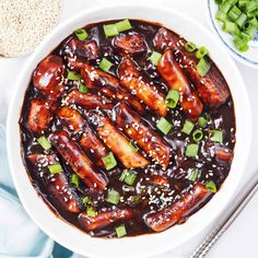 a white bowl filled with meat covered in sauce and green onions on top of a table